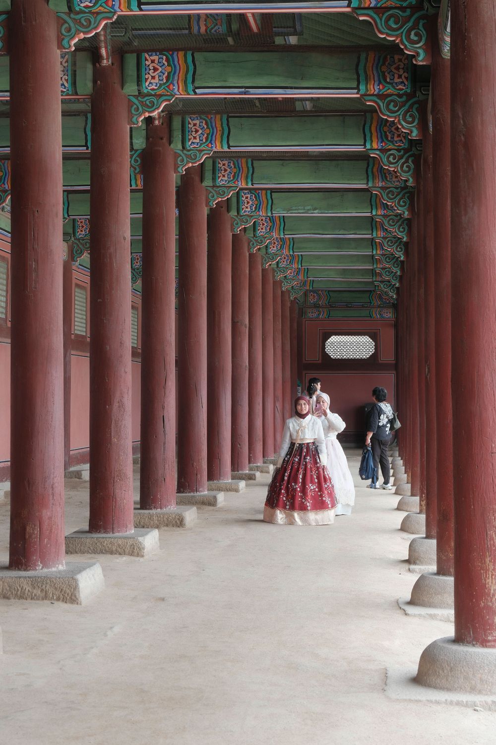 A couple in hanbok walking along a palace corridor